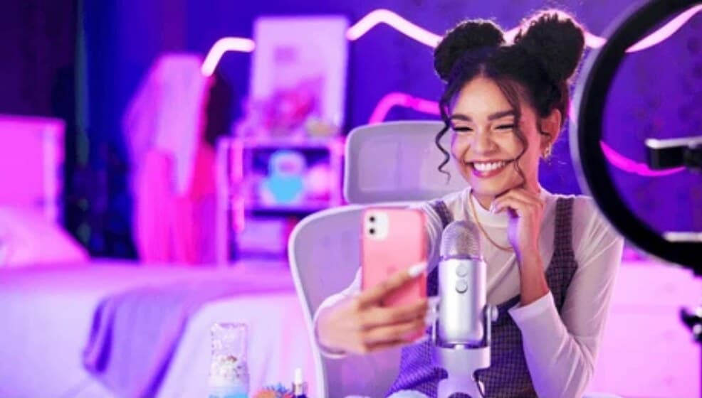Creator filming a selfie video at her streaming setup with a ring light and microphone
